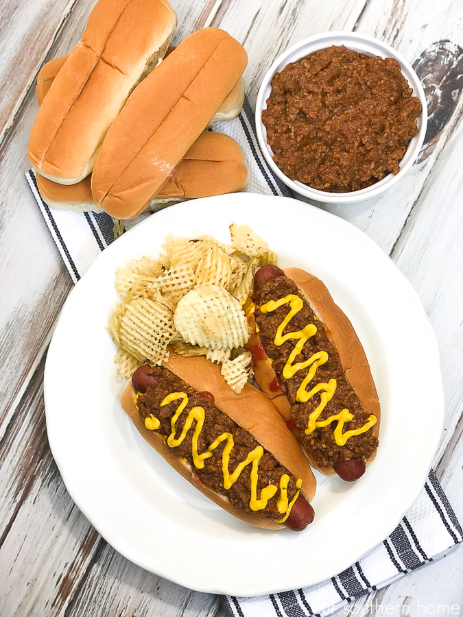hot dogs with chili and mustard on a white plate with a black and white striped towel