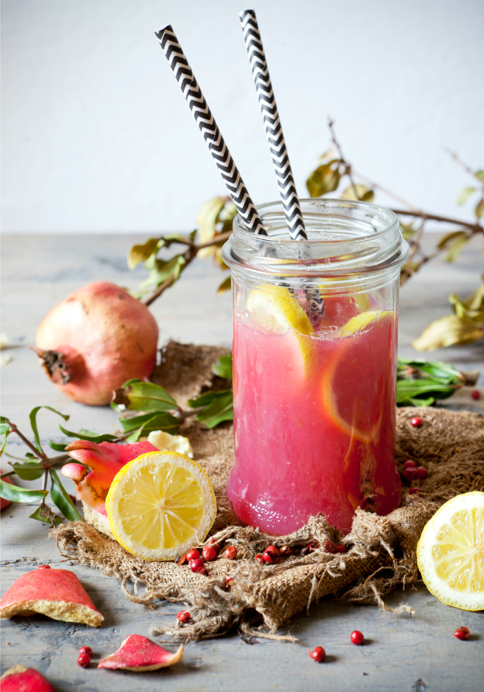 pomegranate and lemon smoothie on glass jar with two striped straw on rustic background with lemon slices and burlap