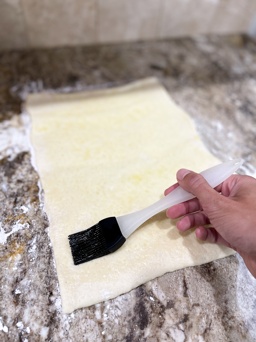 roll of pizza dough being brushed with oil