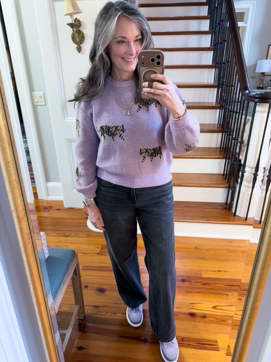 Woman wearing a lilac sweater with animal print and jeans, taking a mirror selfie.
