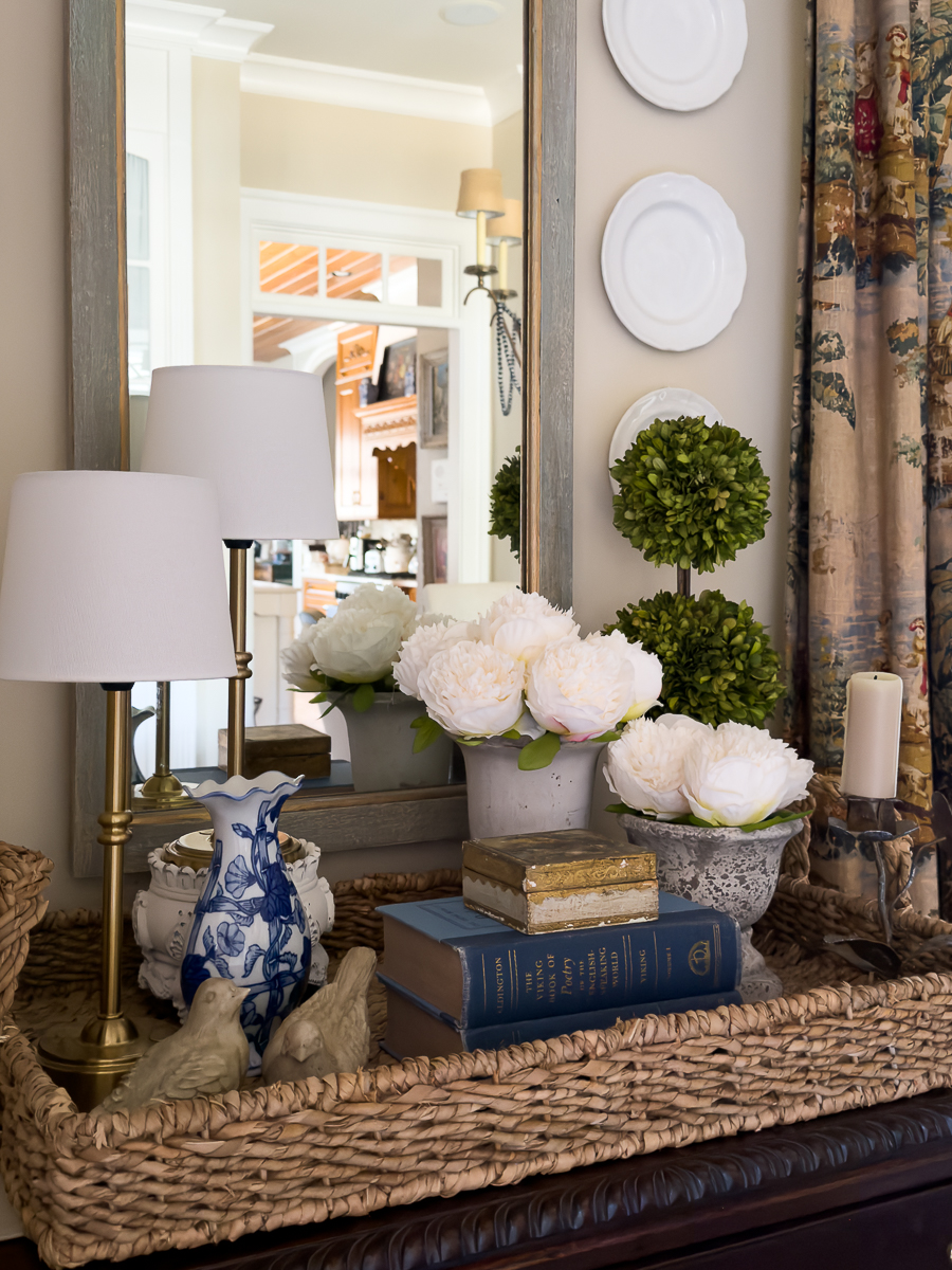 Woven tray styled with vintage books, peonies, brass lamps, and blue and white vase.