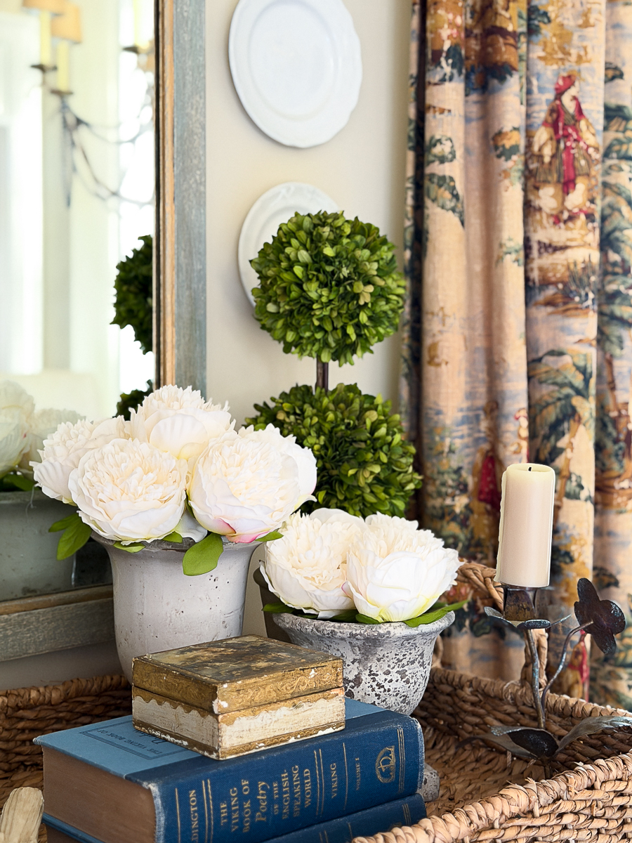 Close-up of thrifted vintage decor styled with peonies and stacked books in woven tray.