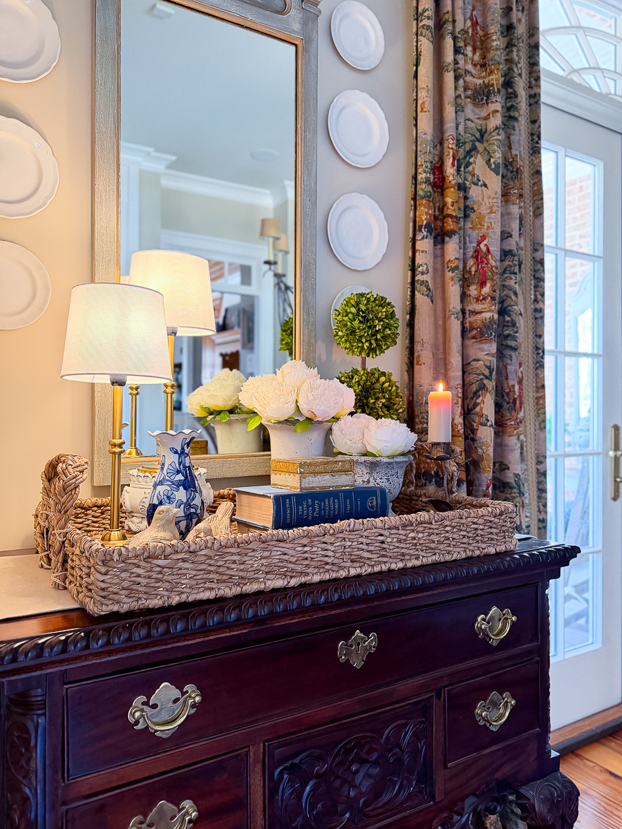Evening spring vignette with candlelight, peonies, vintage books, and woven tray.