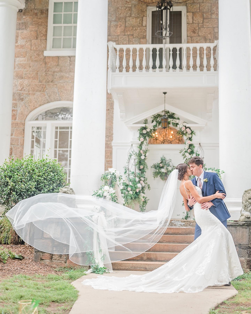 couple in wedding attire in from of mansion